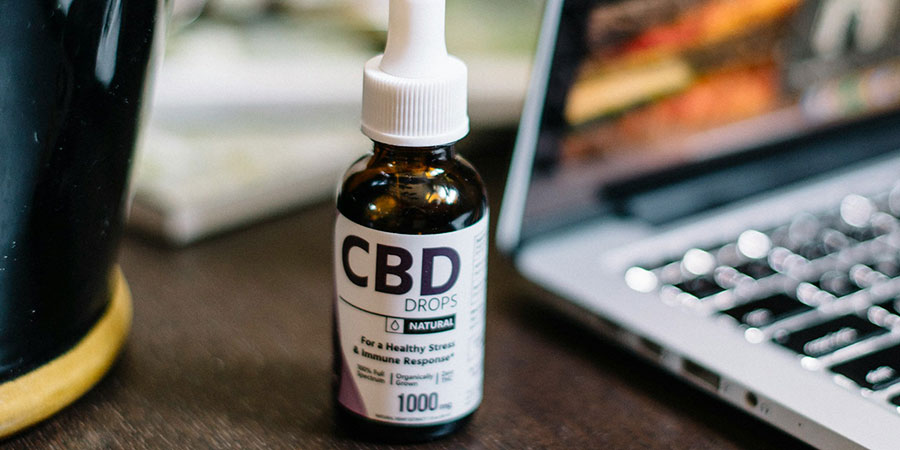 close up view of a small bottle of CBD drops beside a laptop on top of a wooden table