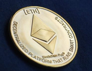 Ethereum symbol debossed on a gold coin on top of a navy blue fabric