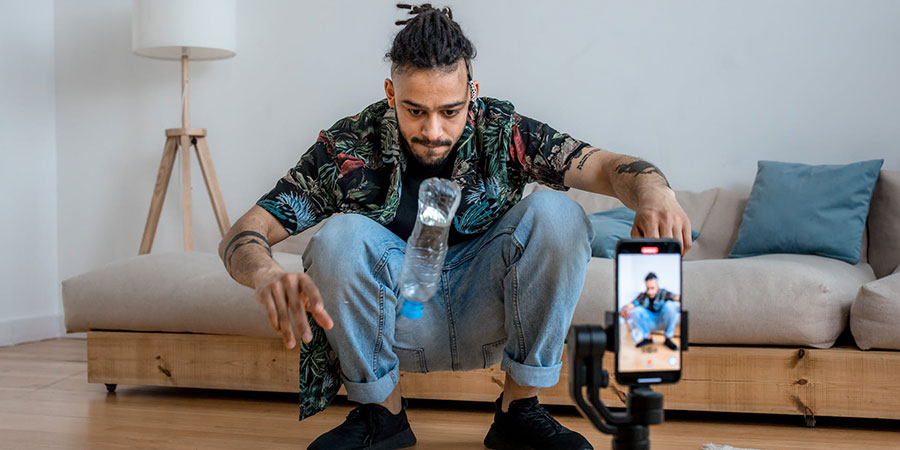 a man doing the bottle flip challenge in his living room while recording himself with his smartphone