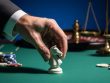 Suited hand placing a white chess knight on green casino felt beside unbranded chips, with a blurred roulette wheel and out-of-focus scales of justice in the background, representing strategy and regulatory compliance in online casino marketing.